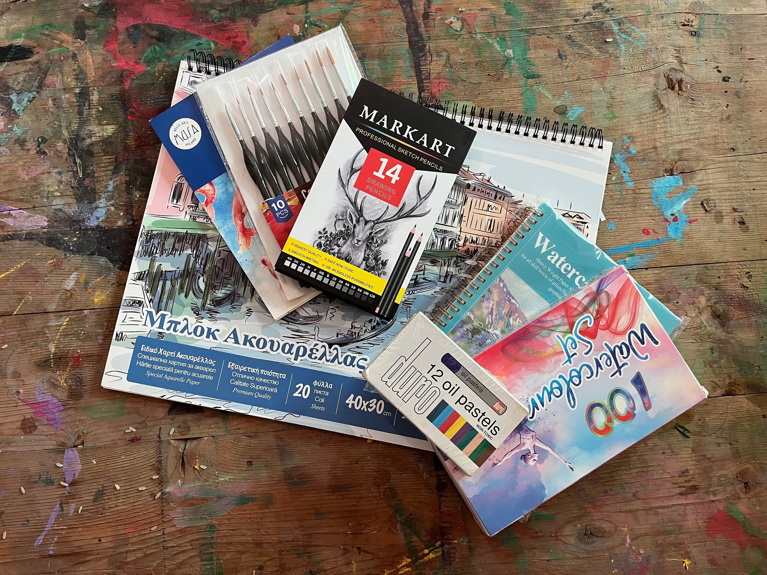 Various art supplies including watercolor paper, oil pastels, sketch pencils, and a drawing pad.
